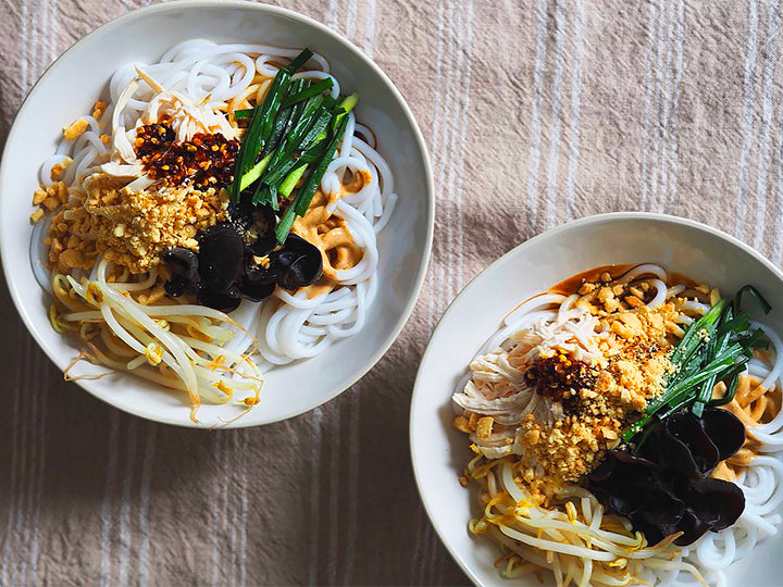 two bowls of cooked Yunnan rice noodles with mushroom, chive and peanut toppings
