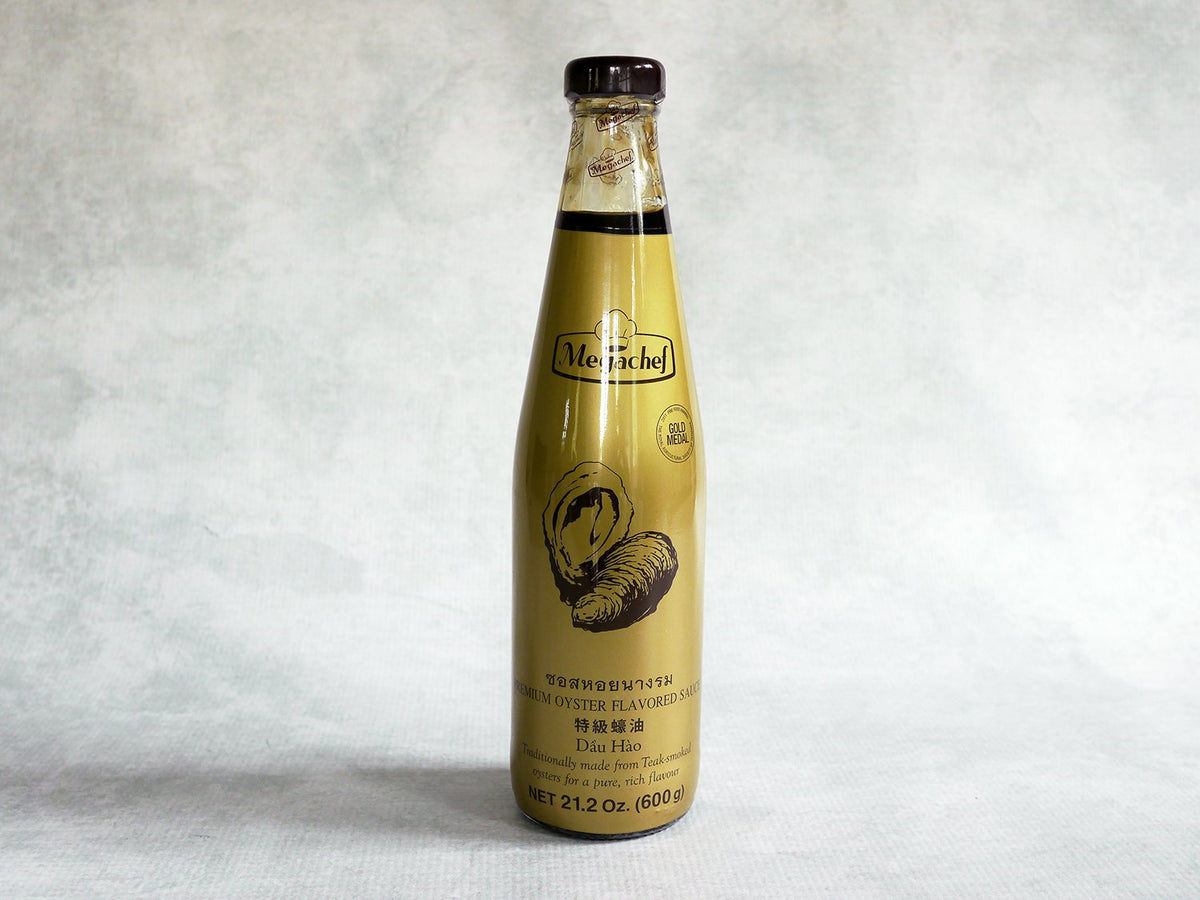 a glass bottle of oyster sauce with a gold label and a drawing of oysters