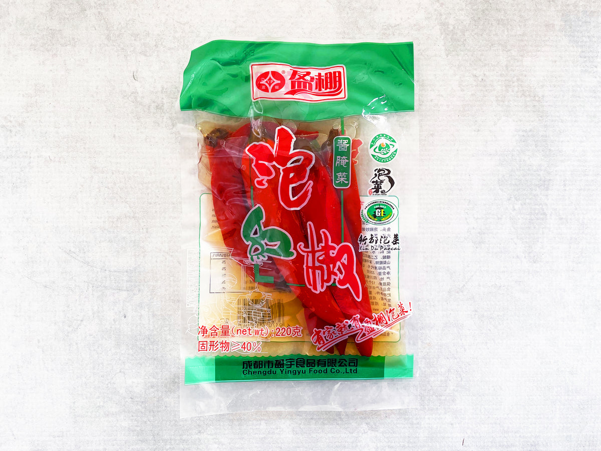A clear plastic bag showing long red pickled chilies in a brine