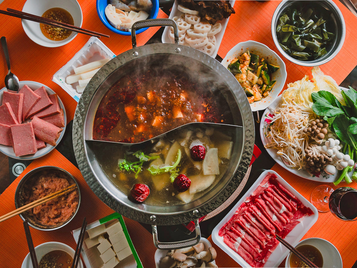 a hot pot with two kinds of soup surrounded by hot pot ingredients on an orange background