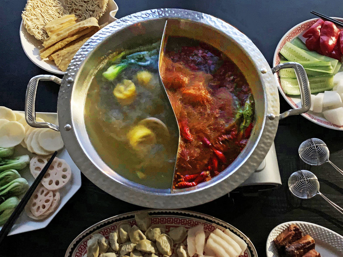a hot pot with two kinds of soup surrounded by hot pot ingredients on a black background