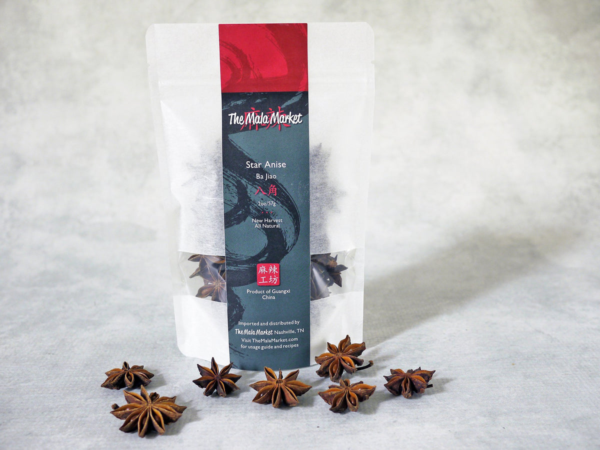 several whole flower-shaped star anise in front of a white kraft bag