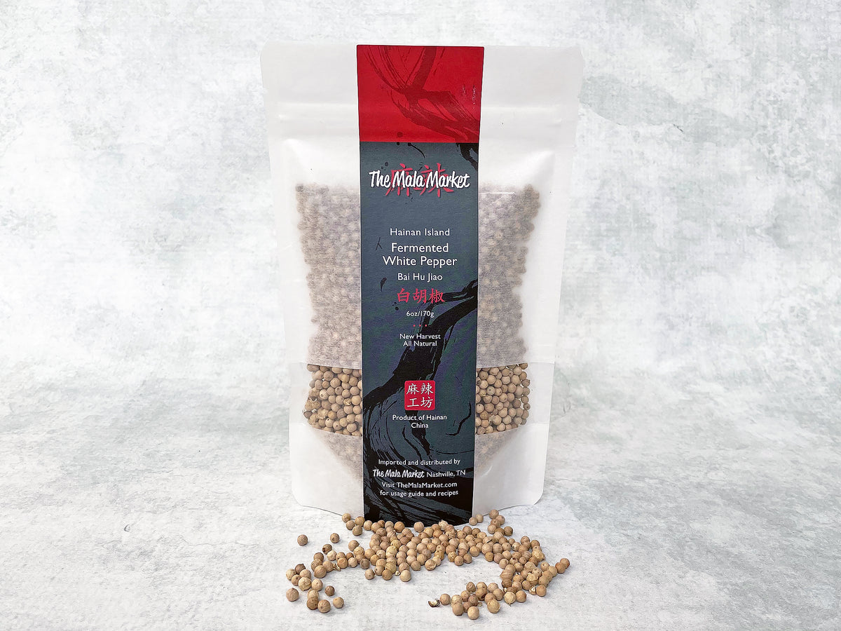 a white kraft bag of fermented white peppercorns from Hainan Island and some loose peppercorns displayed in front of the bag