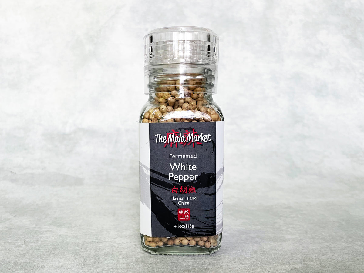 a square glass jar of white peppercorns with an acrylic grinder top