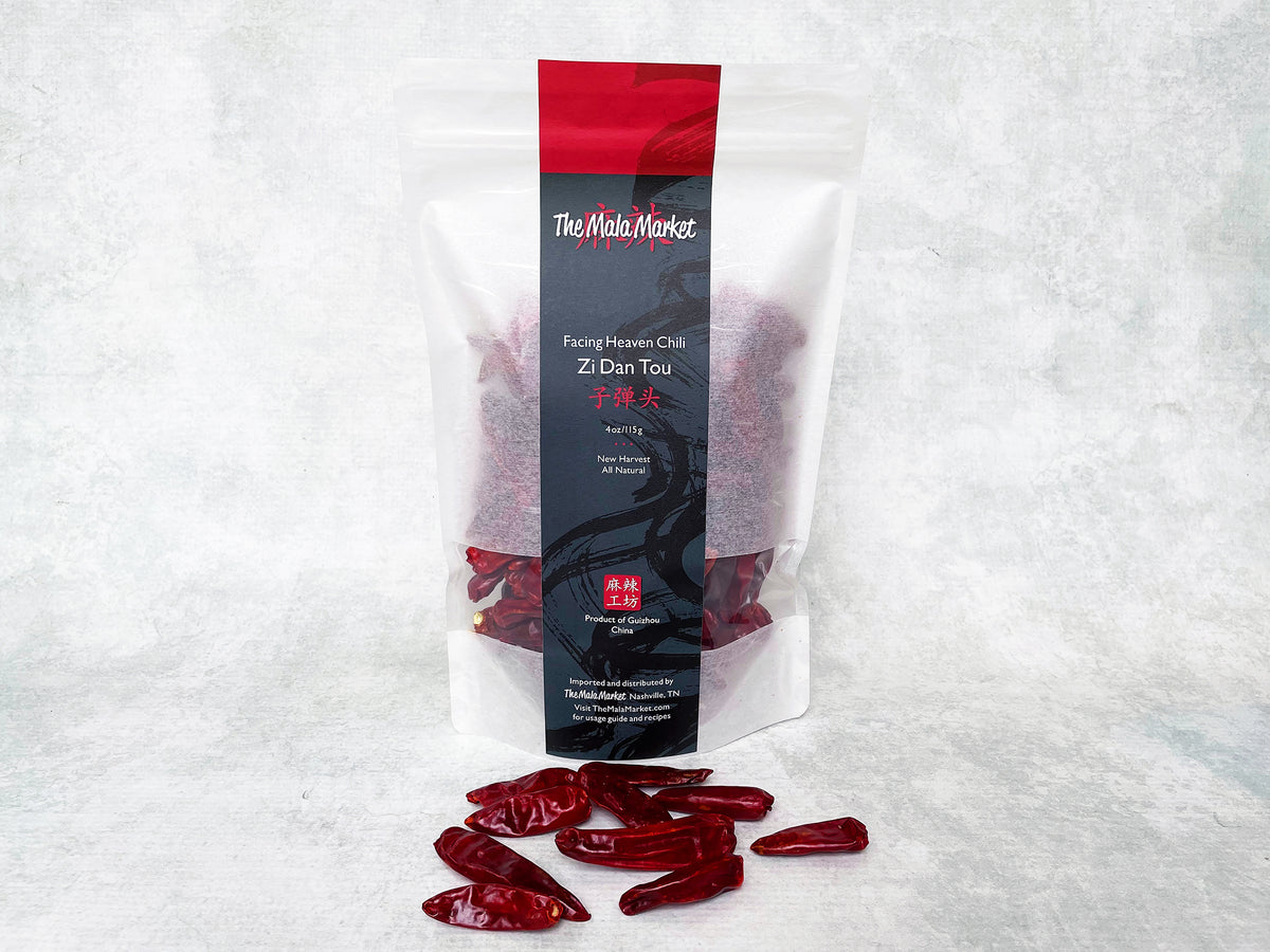 a tall white kraft bag of facing heaven zi dan tou chilies and several dried facing heaven chilies displayed in front of the bag 